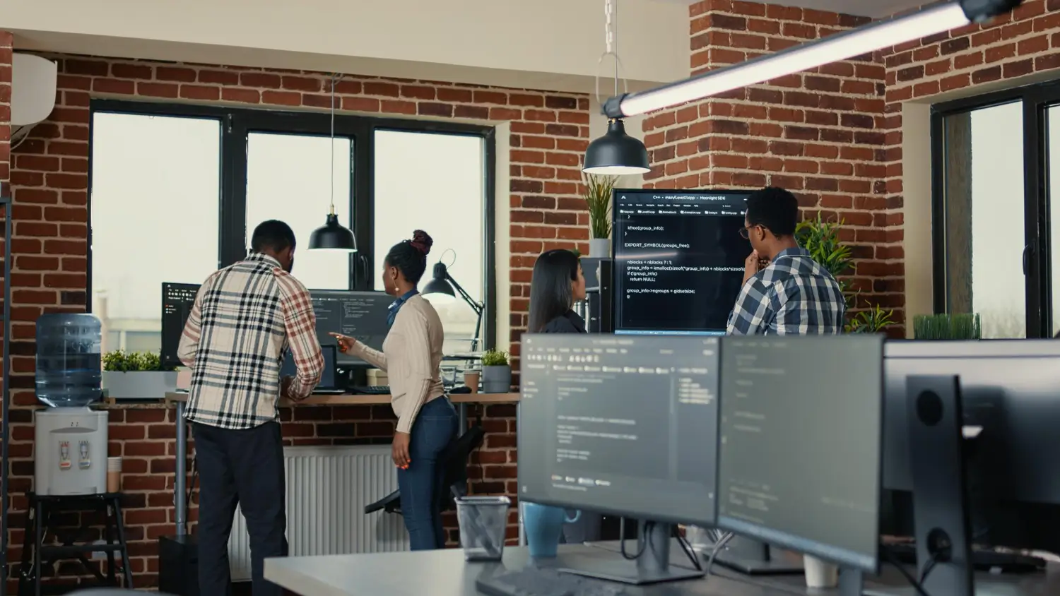 Software development team analyzing code on multiple screens inside an office